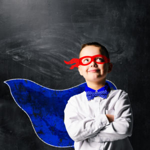 school boy wearing a superhero costume with blackboard behind him